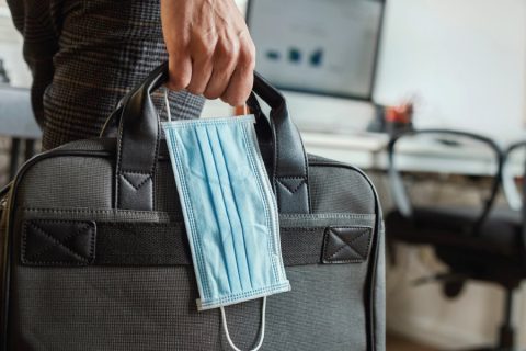Man holding a covid mask next to a suitcase.
