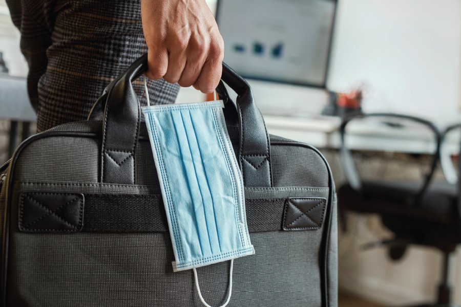 Man holding a covid mask next to a suitcase.