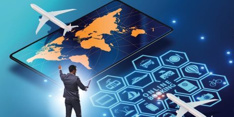 A digital representation of global travel and online booking tools. The image showcases a man standing in front of a large tablet screen displaying a world map in orange and blue tones. Surrounding the map are hexagonal icons symbolizing travel services such as flights, hotels, and transportation, all connected to a futuristic "Online Booking" interface. Two airplanes appear to fly above the scene, enhancing the theme of worldwide travel and digital connectivity.