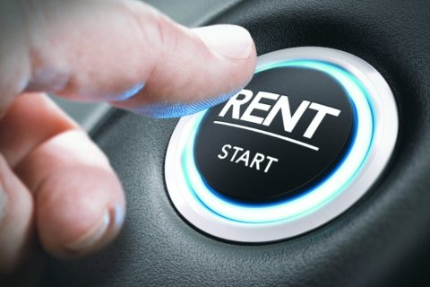 A close-up of a hand pressing a button labeled "RENT" with "START" written underneath it, surrounded by a glowing blue light. The button is set into a sleek surface, resembling a car dashboard, symbolizing the concept of starting or accessing a rental vehicle. The image conveys modern car rental services or ease of access.