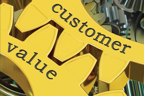 A close-up of two interlocking golden gears with the words "customer" and "value" engraved on them. The gears are surrounded by metallic components, symbolizing the interconnected nature of customer satisfaction and value creation within a business or organizational system. The vibrant gold color conveys importance and quality.