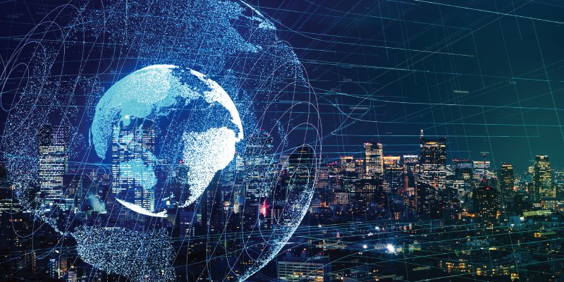 A digitally rendered image of Earth, appearing as a glowing, wireframe globe, set against a backdrop of a cityscape illuminated at night. Overlaying the scene are network lines and nodes, symbolizing global connectivity and data networks.