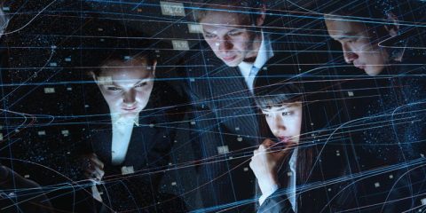 A group of professionals in formal attire deeply focused on data or technology, with a digital overlay of interconnected lines and numerical data. The image conveys themes of innovation, teamwork, and analytics in a high-tech or corporate environment. The glowing blue lines and data points add a futuristic and dynamic element to the visual.