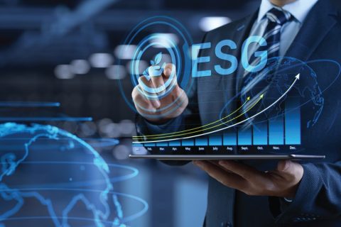 A business professional in a suit holding a tablet with holographic visuals of "ESG" (Environmental, Social, Governance) prominently displayed. The visuals include a glowing leaf icon, a graph with upward-trending lines labeled by months, and a digital globe, symbolizing sustainable growth, global responsibility, and data-driven ESG strategies. The futuristic design emphasizes technology and corporate focus on sustainability.