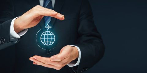 A business professional in a suit cupping their hands around a glowing icon of a globe with a small airplane flying over it. The icon symbolizes global travel and connectivity, with a focus on protection or nurturing of the concept. The dark background highlights the bright, futuristic design, emphasizing innovation in the travel or aviation industry.