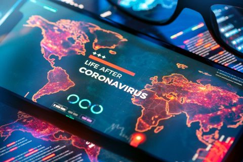 A glowing digital display shows a world map with regions illuminated in red, depicting the global impact of COVID-19. The text "LIFE AFTER CORONAVIRUS" appears prominently in bold white and red. Surrounding the map are futuristic data graphics, charts, and digital icons, creating a theme of post-pandemic priorities and technological adaptation in a globally connected world.