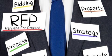 A business professional dressed in a dark suit and blue tie with index cards pinned to the suit. The cards display key business terms such as "RFP: Request For Proposal," "Bidding," "Property," "Process," "Strategy," and "Guide," each written in a bold font with underlining in various colors. The visual emphasizes the critical elements involved in creating and responding to requests for proposals (RFPs) in a structured and strategic manner.