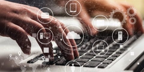 Close-up of hands typing on a laptop keyboard, overlaid with digital icons representing cloud computing, mobile devices, servers, and interconnected systems. The image conveys the concept of technology, data integration, and digital transformation.